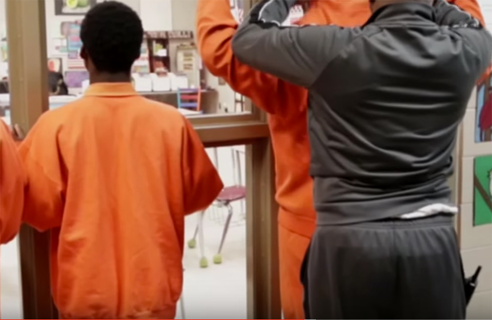 young men in orange prison uniforms being searched