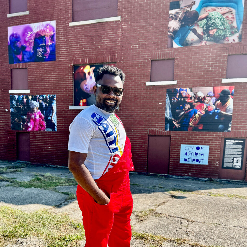 Dieu-Nalio Chery standing infornt of a building displaying his photography